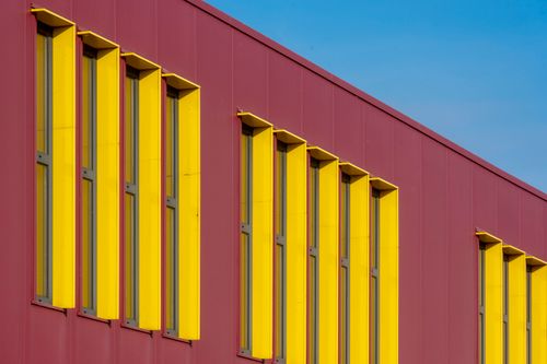 Free A striking modern architectural facade featuring vibrant yellow and red panels with tall windows. Stock Photo