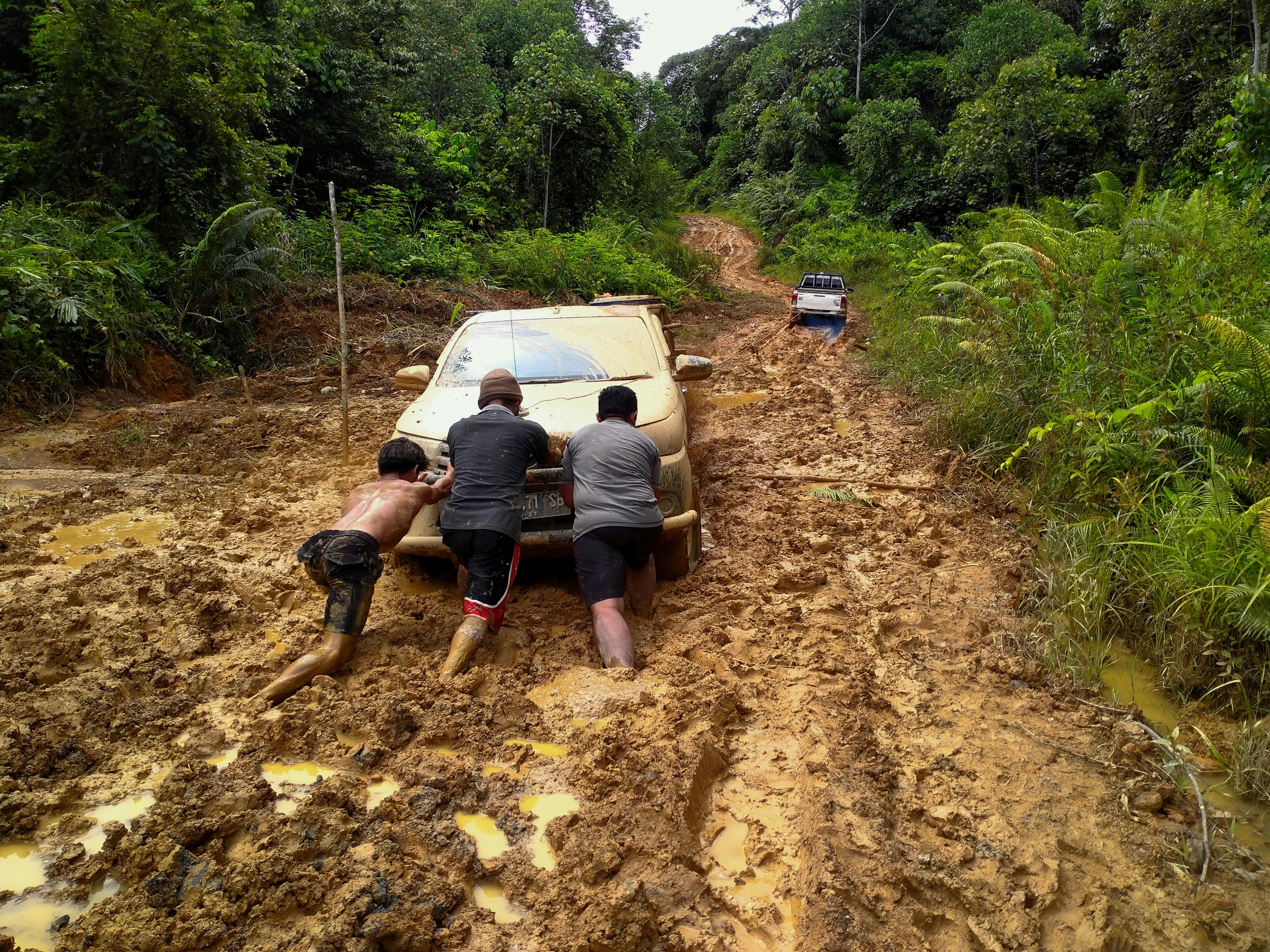 Three men push a car through a muddy forest road in North Kalimantan, Indonesia.
