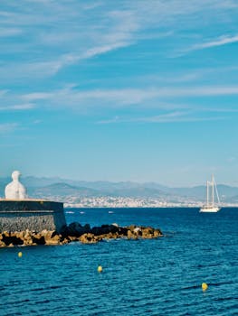 Explore the scenic Antibes harbor with a majestic sculpture overlooking sailboats on the azure sea.