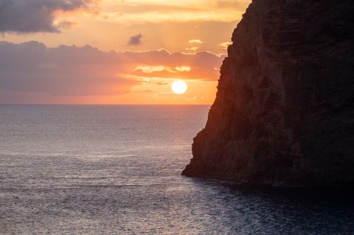Free Breathtaking view of a vibrant sunset over the ocean with a dramatic rocky cliff in the foreground. Stock Photo