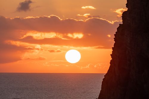 Free Dramatic sunset over ocean with silhouetted cliffs and vibrant orange sky. Stock Photo