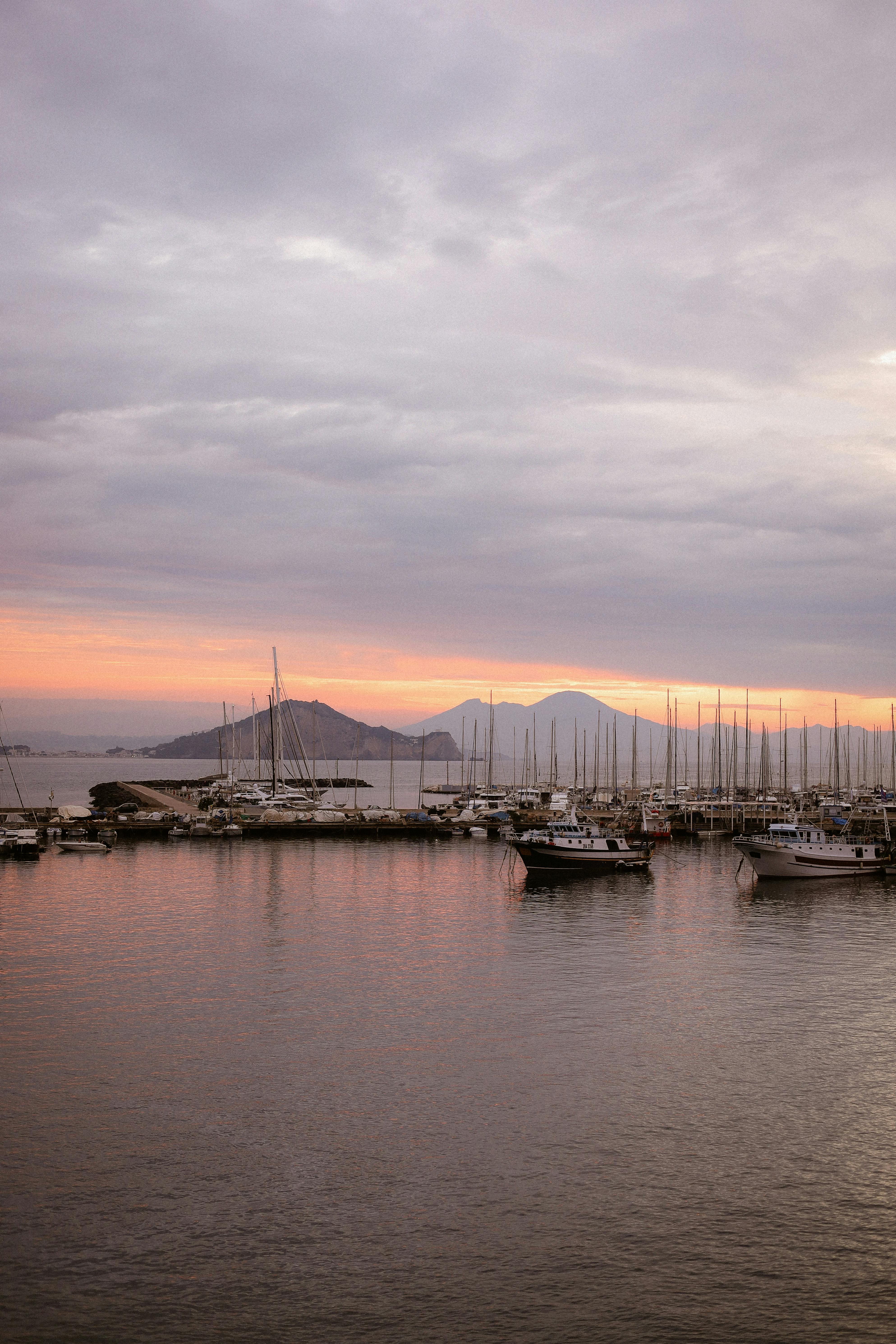 Peaceful harbor scene at twilight with boats, mountains, and a vivid sunset sky.
