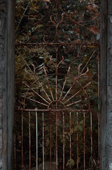 A weathered iron gate stands amidst lush foliage in a serene garden.