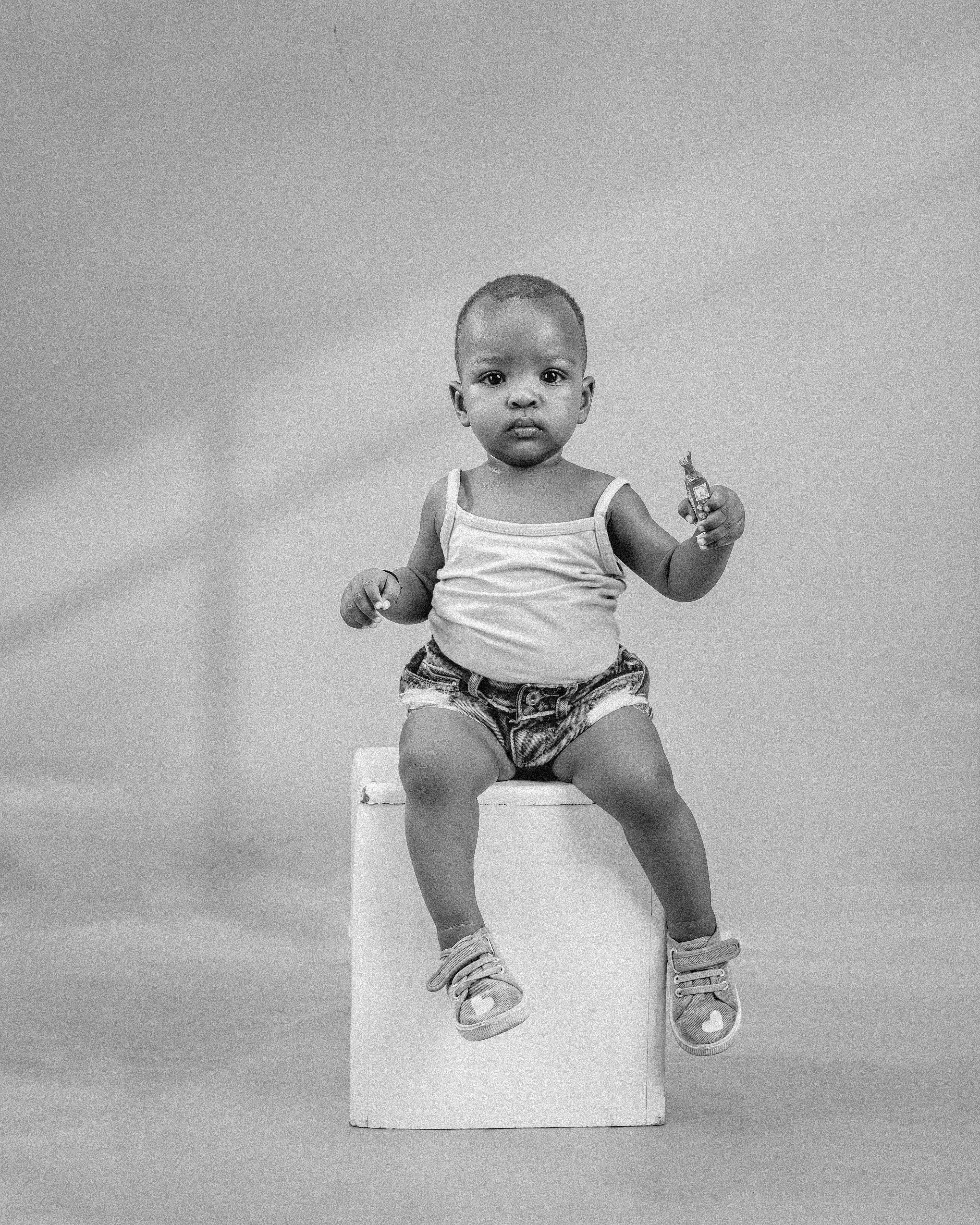 Charming baby sitting on a stool in a black and white studio portrait.