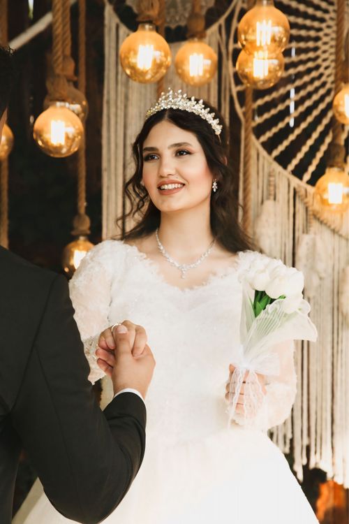Free Beautiful bride in white gown holding bouquet indoors with warm lighting. Stock Photo