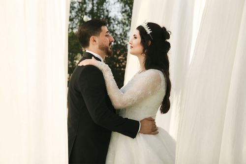 Free Romantic outdoor wedding portrait of a bride and groom embracing between elegant curtains. Stock Photo