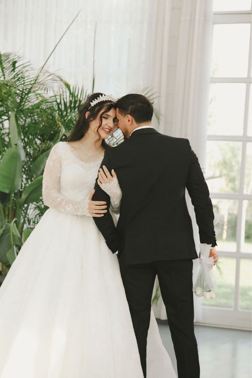 Free Bride and groom lovingly embrace indoors, with natural light and greenery. Stock Photo