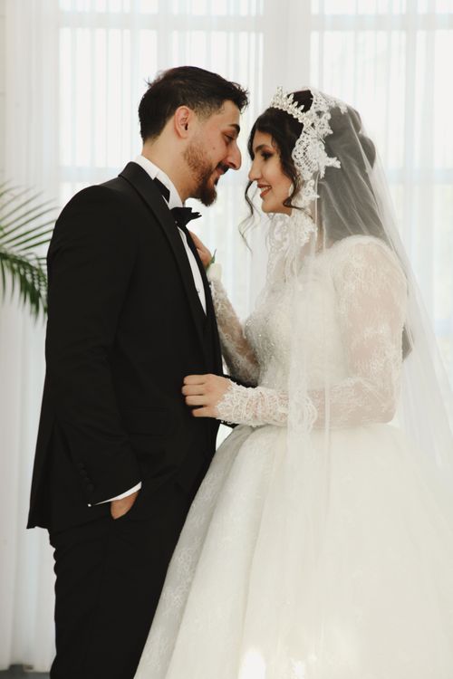 Free Bride and groom in elegant attire sharing a tender moment at an indoor wedding. Stock Photo