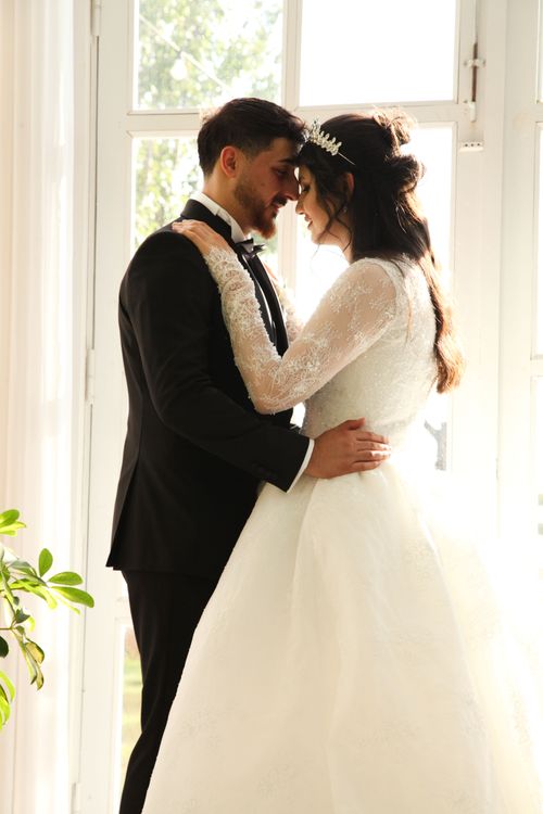 Free Elegant couple embracing on their wedding day with natural light pouring in. Stock Photo