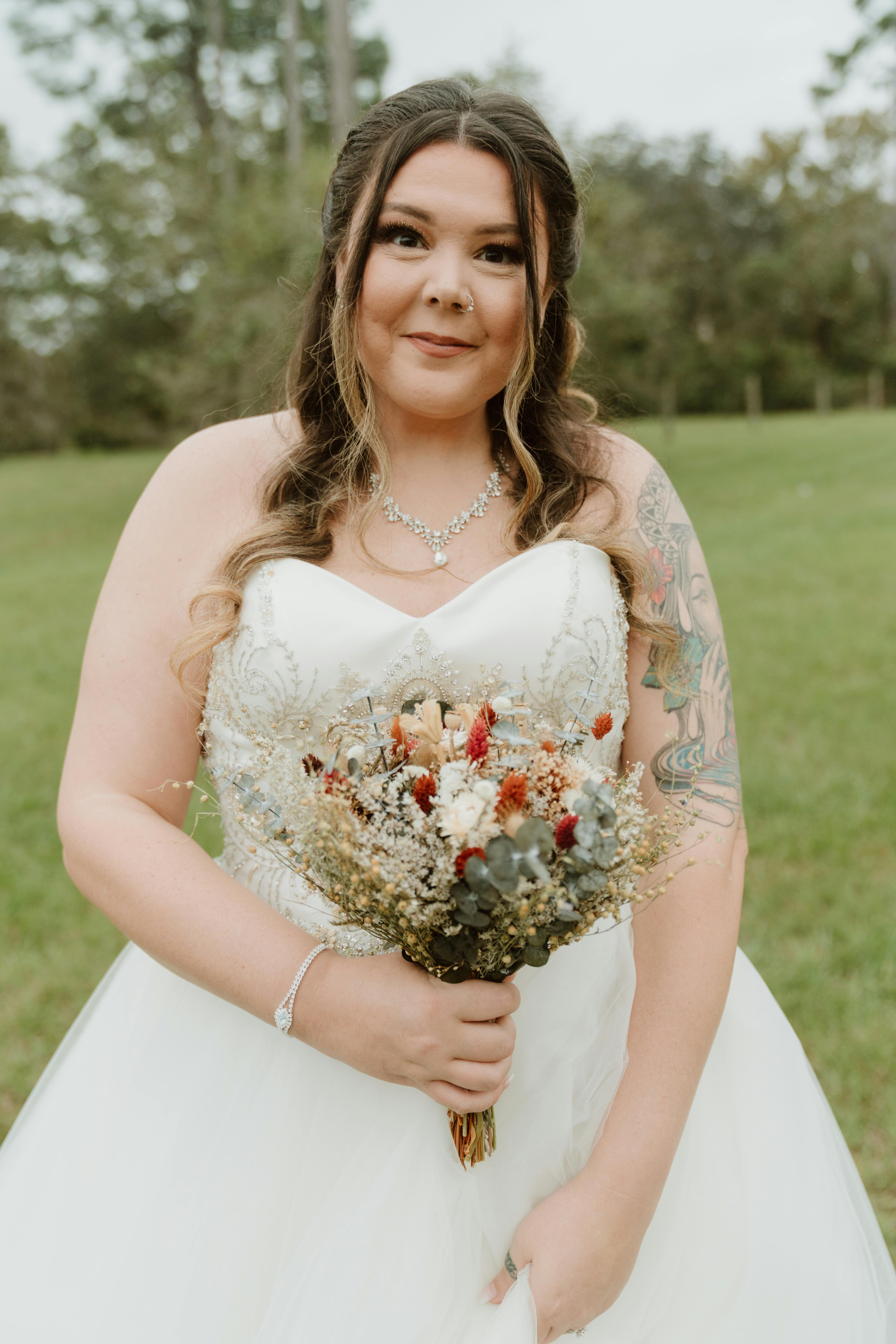 A smiling bride with floral bouquet in an outdoor wedding ceremony.