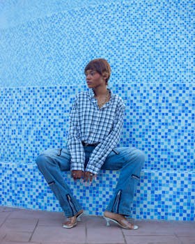 Stylish adult woman in denim and plaid sits by a blue mosaic wall.
