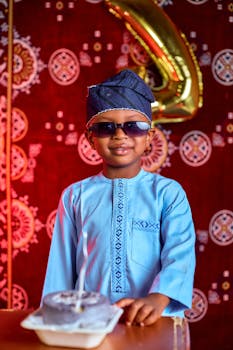 A young boy in traditional attire celebrates his birthday with a cake and decorations.