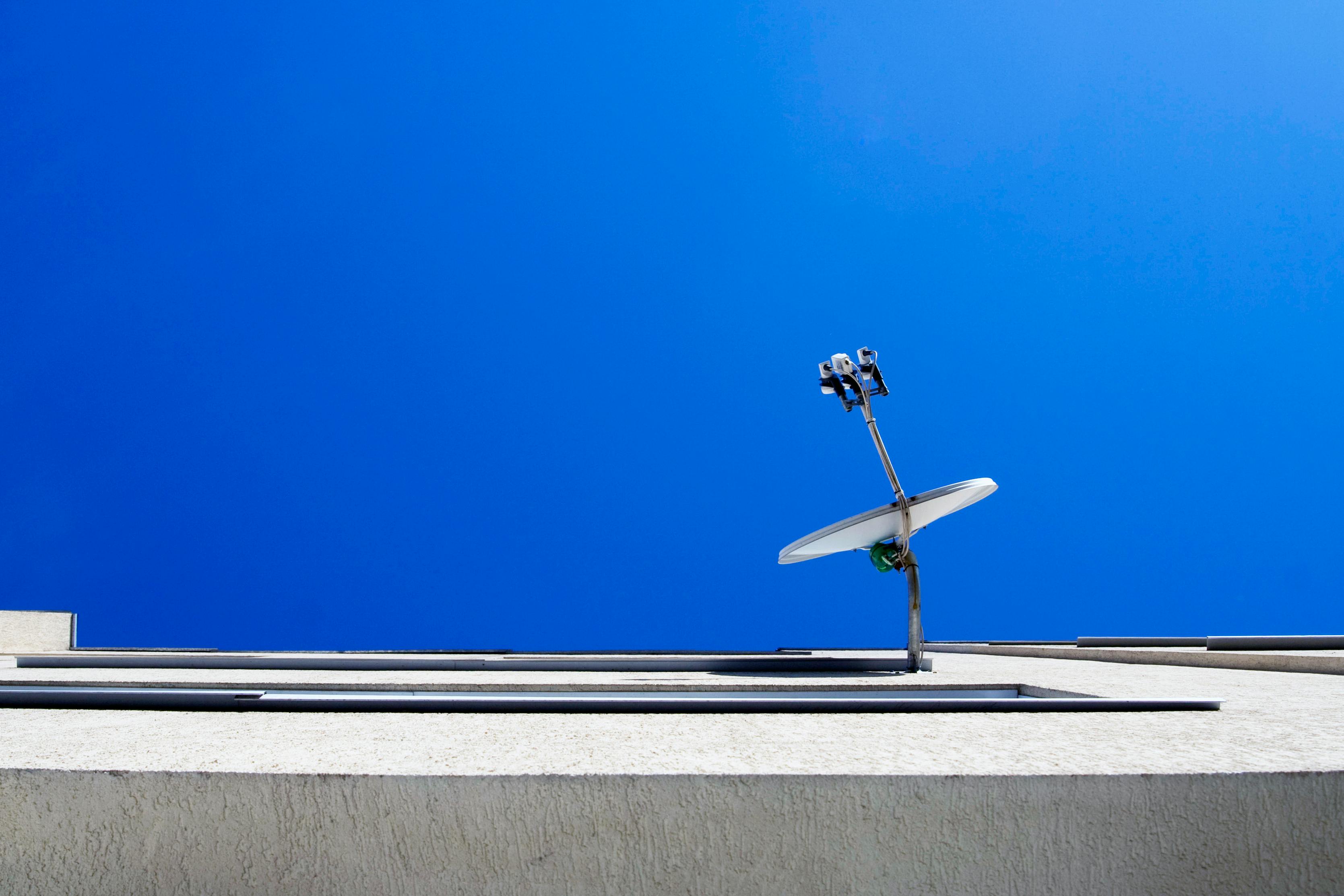 免费 从低角度拍摄的现代建筑上的卫星天线，背景是湛蓝的天空。 素材图片