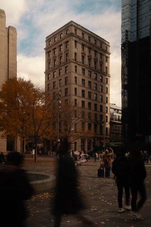 Free Blurred pedestrians and autumn trees in a city square with historic buildings. Stock Photo