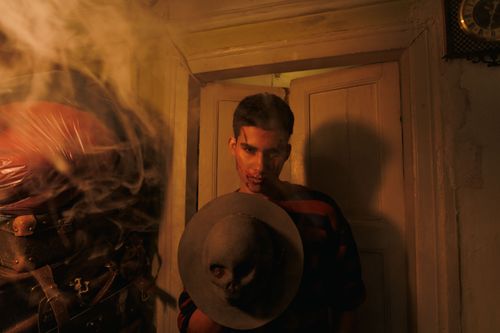 Free A man in a dimly lit room holds a hat adorned with a skull, surrounded by smoke. Stock Photo