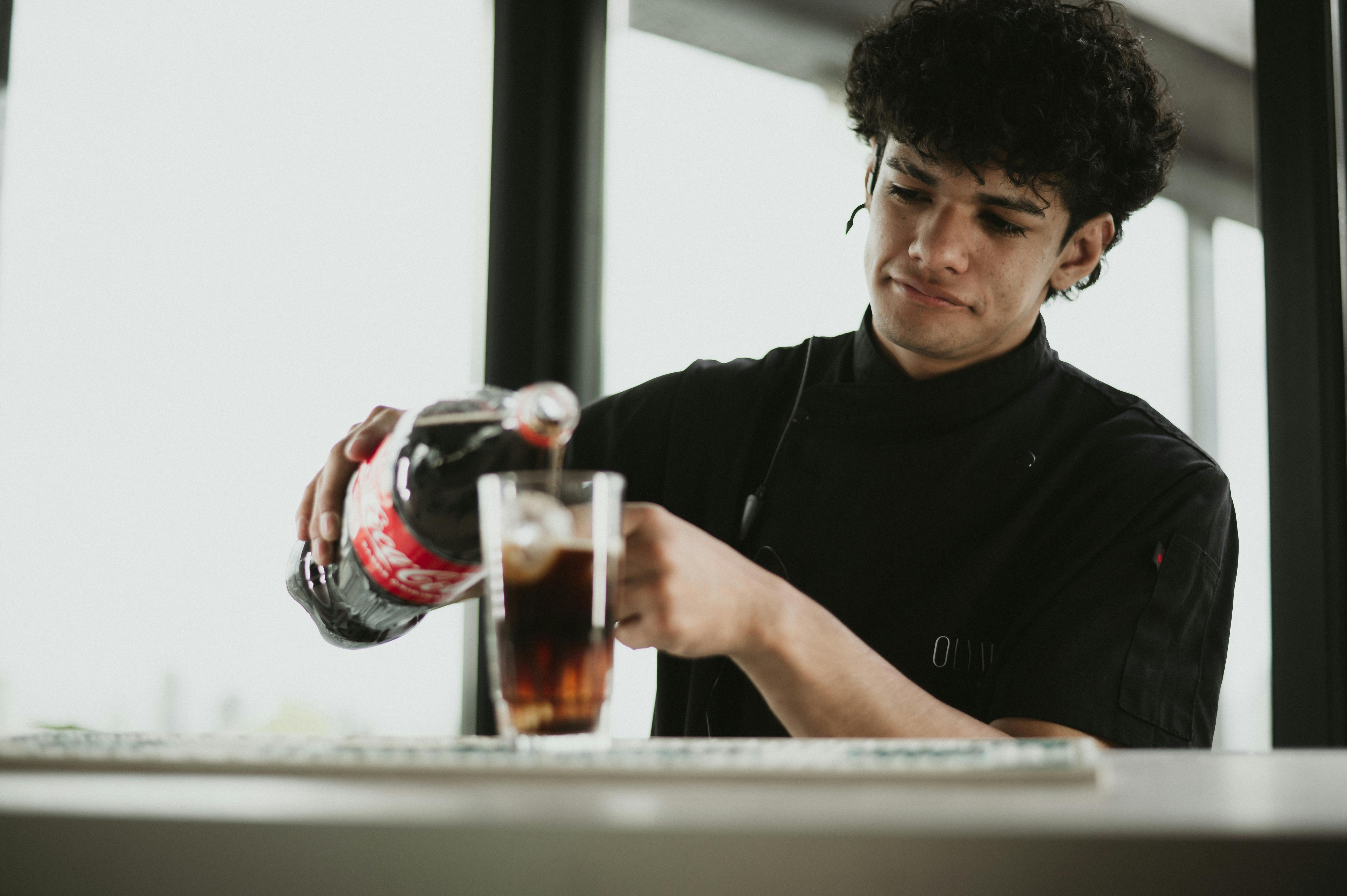 Young bartender pouring soda into glass at a Buenos Aires cafe. Natural light setting.