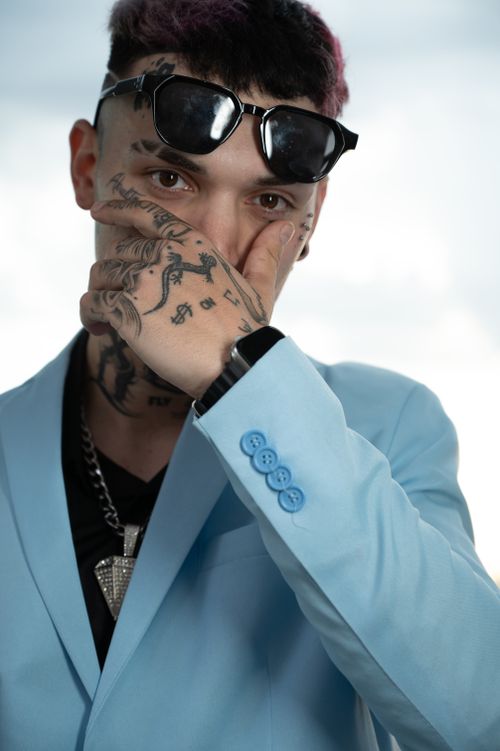 Free Stylish portrait of a tattooed man in a light blue suit with sunglasses and hand tattoos. Stock Photo