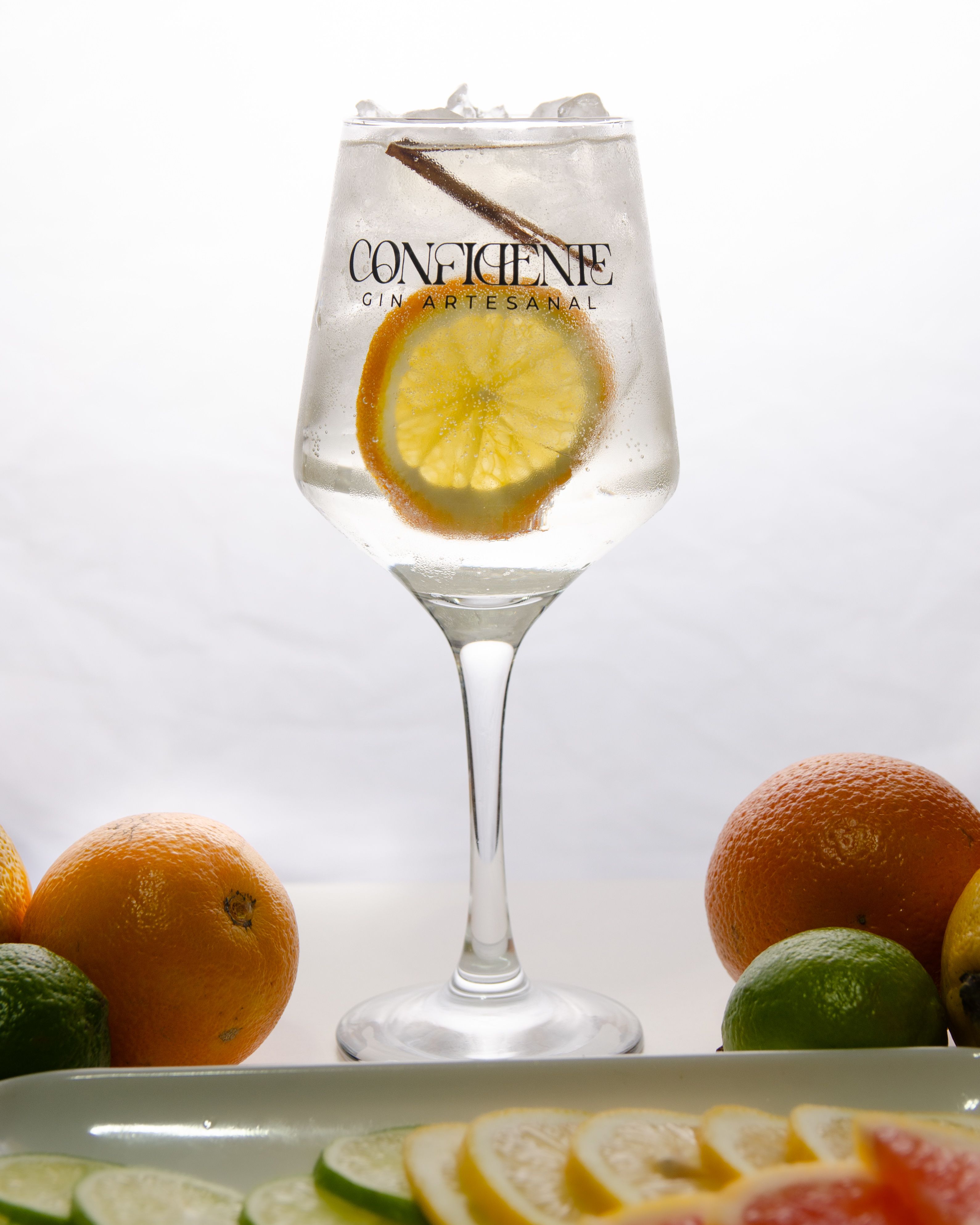 Artisan gin served in a glass with lemon and spices, surrounded by citrus fruits.