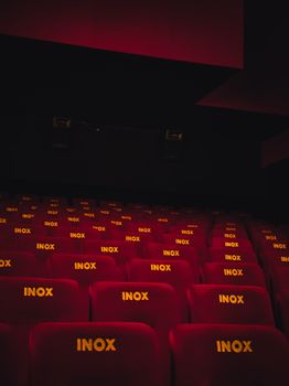 A perspective view of empty red seats in a dimly lit movie theater.