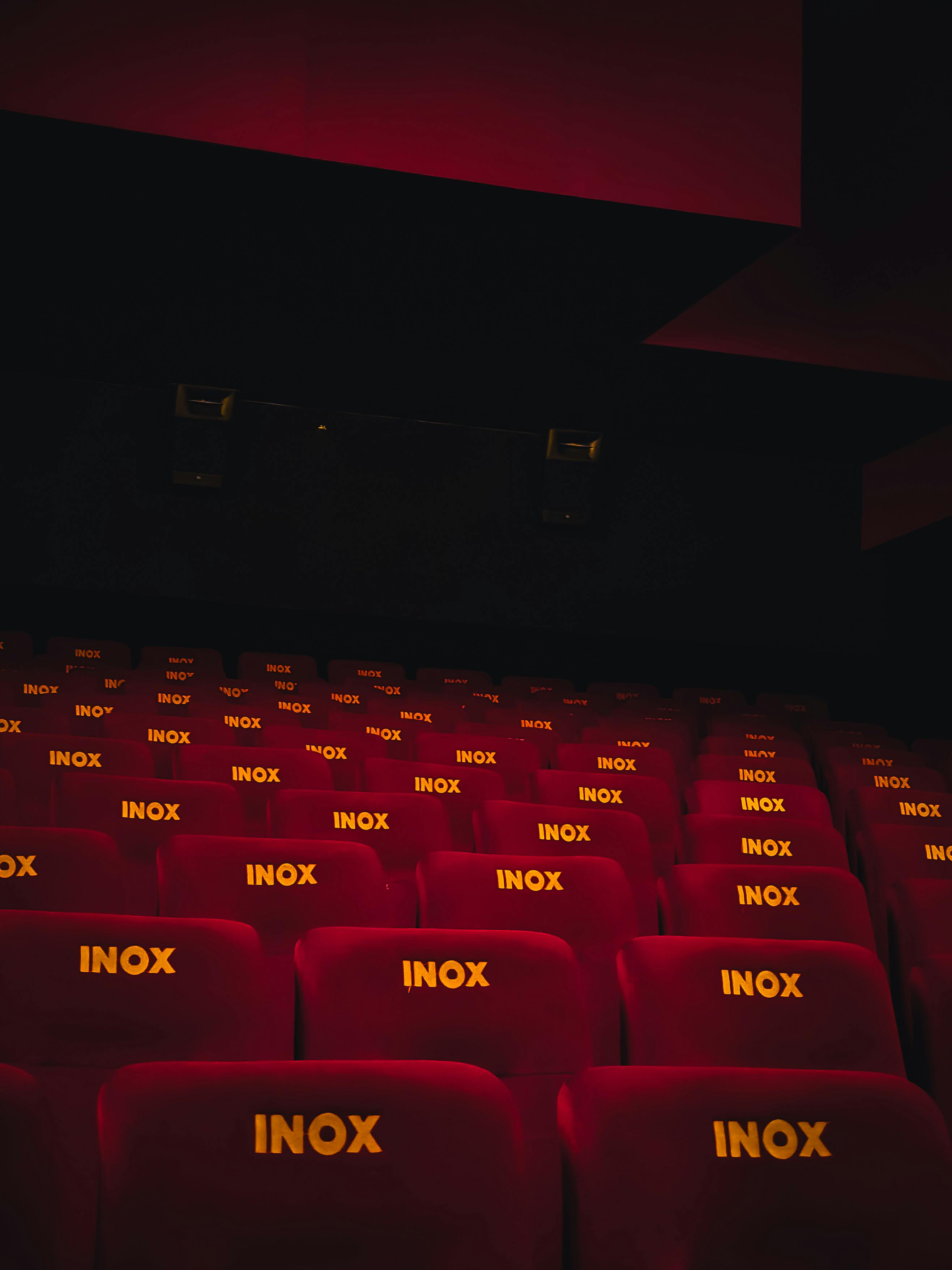 Free A perspective view of empty red seats in a dimly lit movie theater. Stock Photo