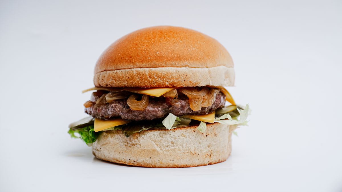 Tall cheeseburger with a soft golden bun, melted cheese, caramelized onions, pickles and lettuce