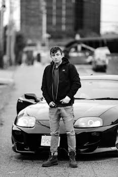 在加拿大的街道上，一名男子自信地站在一辆时尚的豪华车前，背景是单色环境