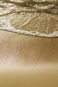 Close-up of gentle waves on a golden sandy beach, capturing serene beach vibes.