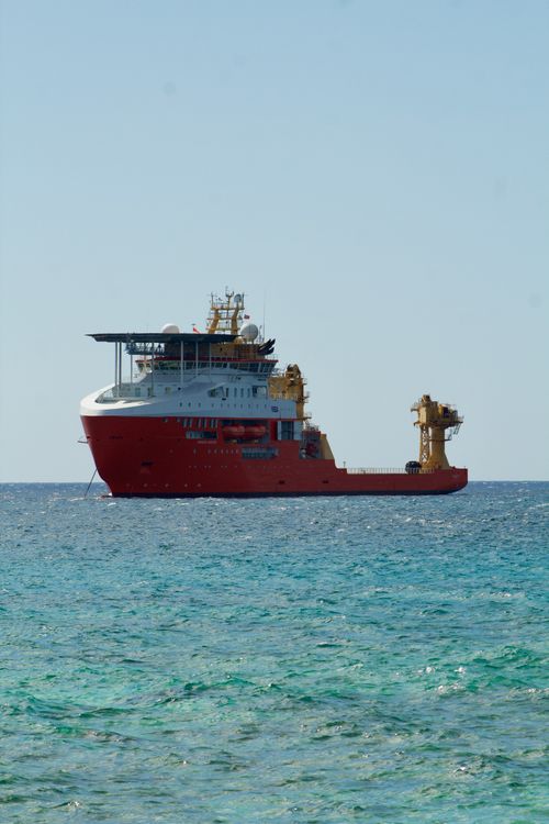 Free A vibrant red cargo ship sailing on a clear blue ocean with a bright sky. Stock Photo