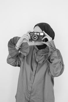 Black and white portrait of a woman in hijab holding a vintage camera.