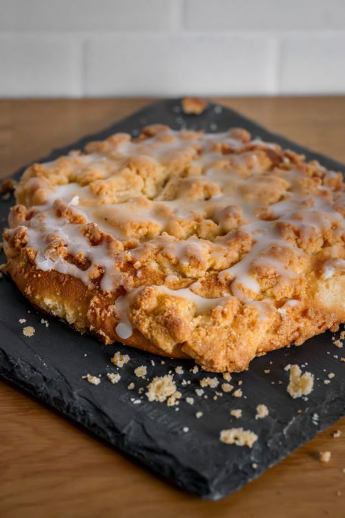 Free Crumbly coffee cake topped with icing glaze on a black slate board. Stock Photo
