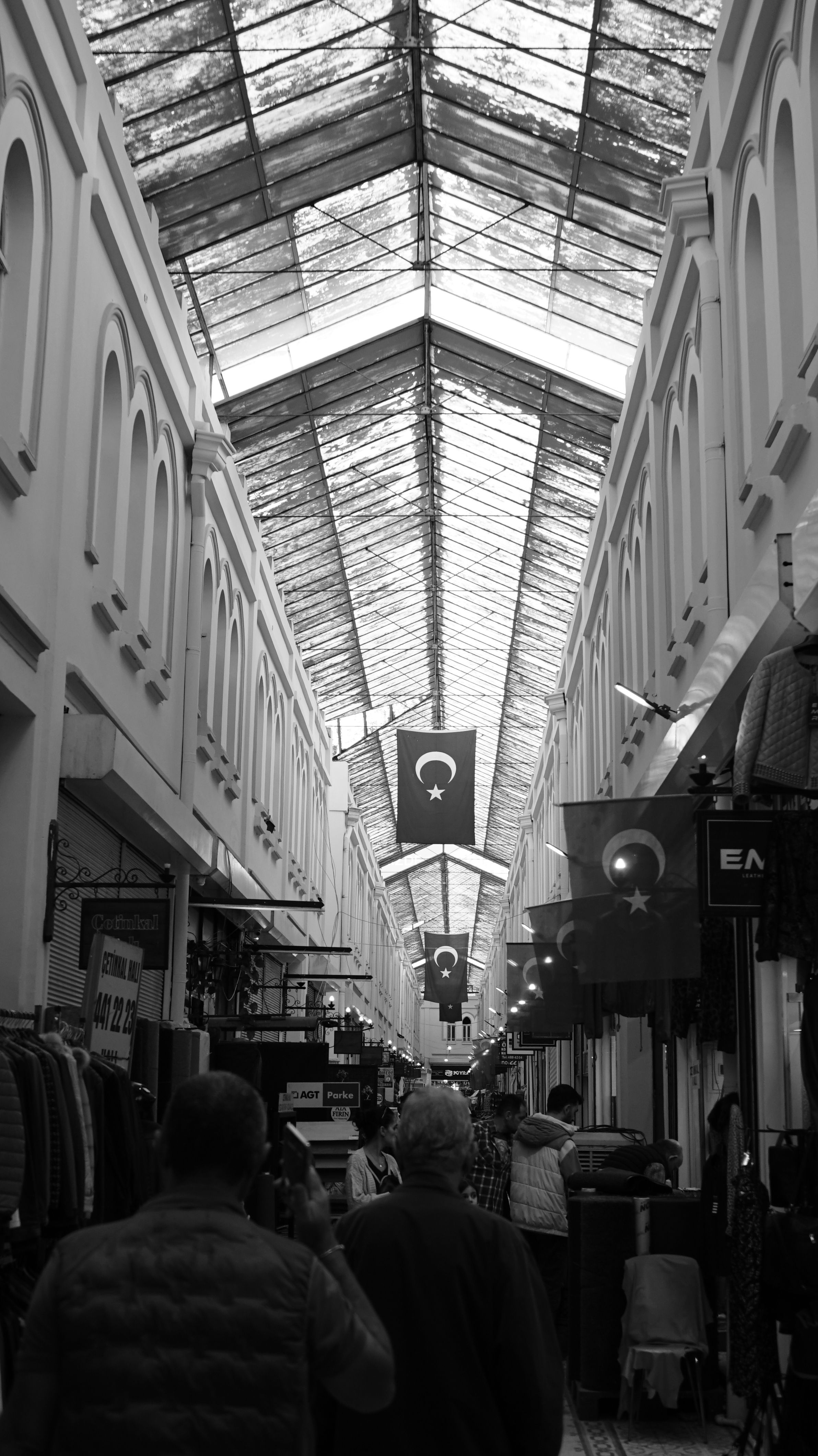 Monochrome view of a bustling Turkish bazaar with flags and arched ceilings.