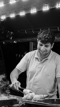 A joyful street vendor grills corn under festive lights at a night market.