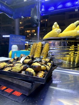 Night-time street food stall showcasing roasted chestnuts and grilled corn cobs under vivid blue lights.