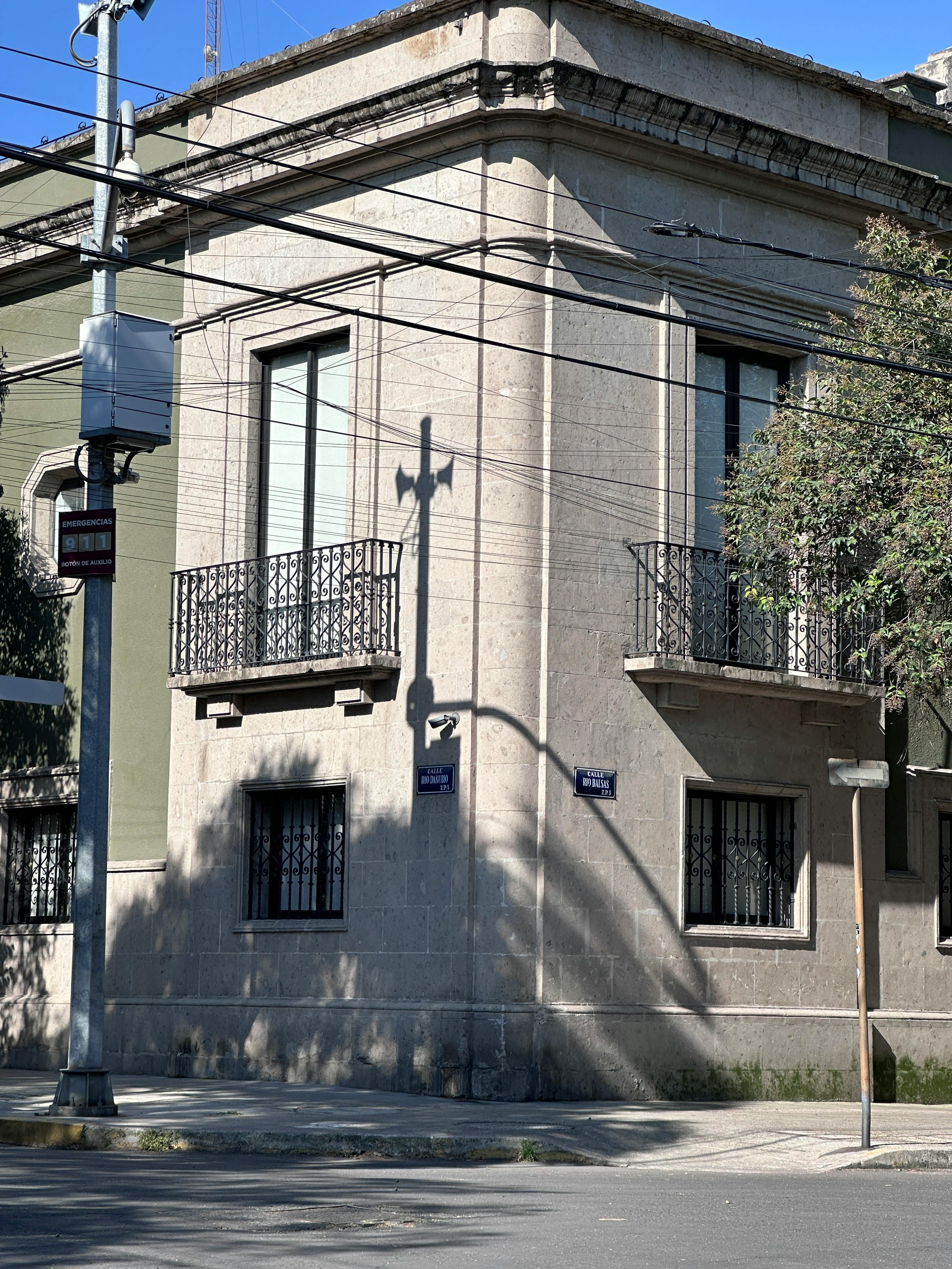 Free Corner building casting shadow with wrought iron balconies and street signs under clear sky. Stock Photo