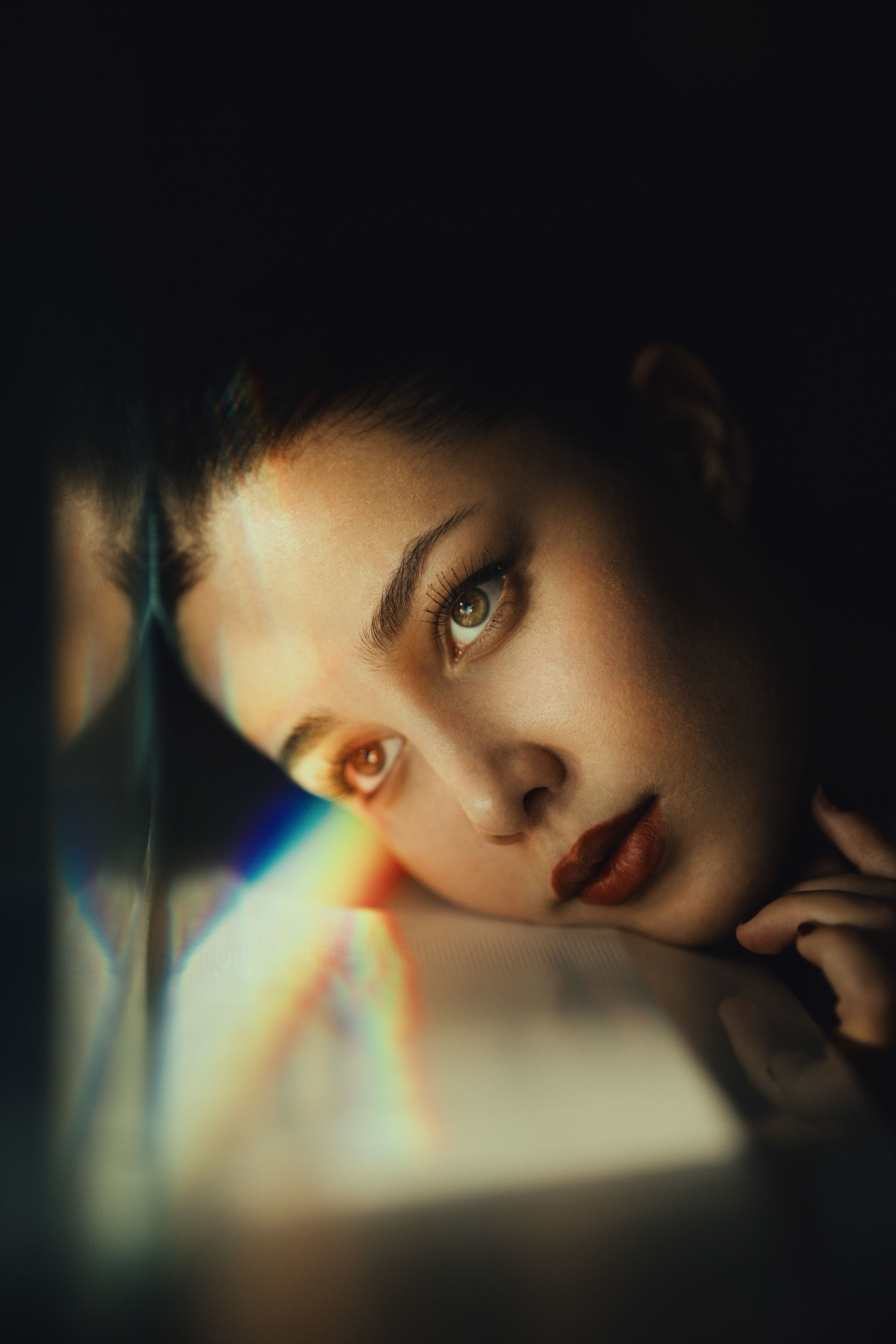 A contemplative woman gazes with prismatic reflections on a dark background.