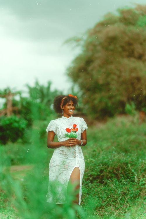 Free Smiling woman in white dress with red flowers in a green, outdoor setting. Stock Photo
