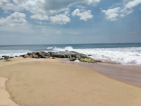 A serene view of Pottuvil Beach with gentle waves and clear skies.