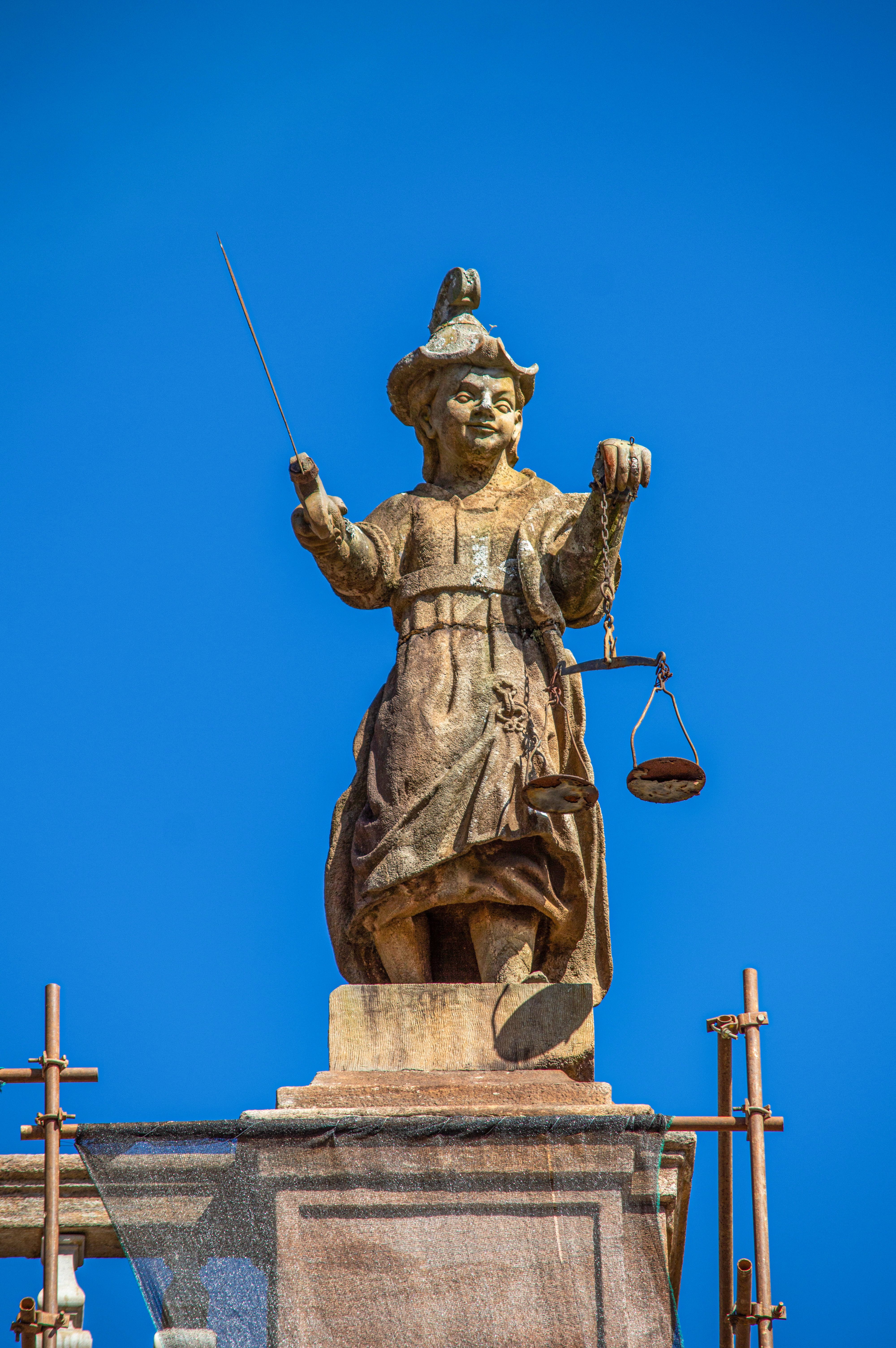 Outdoor statue of Justice holding scales and a sword under a clear sky.