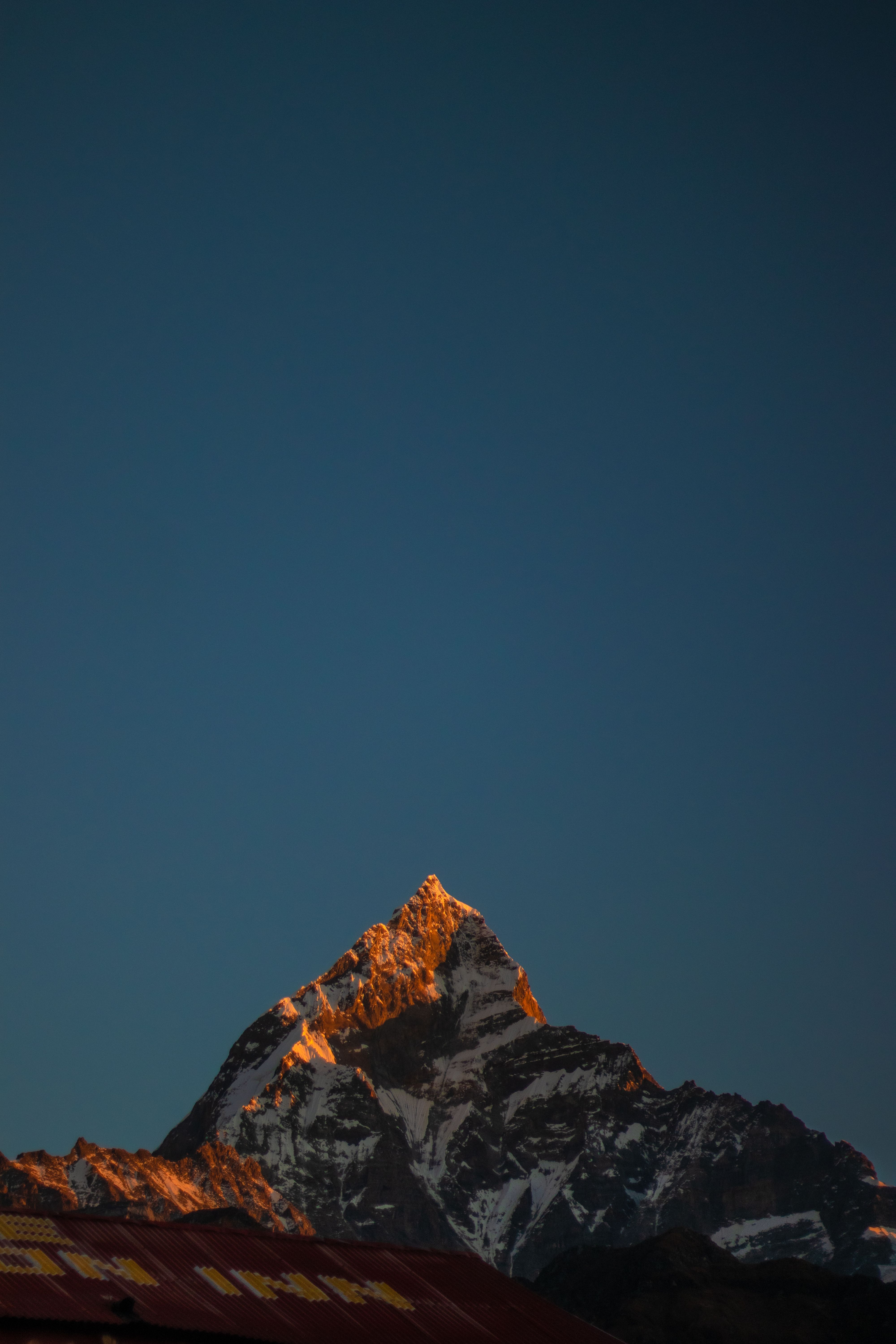 A stunning view of a snow-capped mountain peak illuminated by sunrise light against a clear blue sky.
