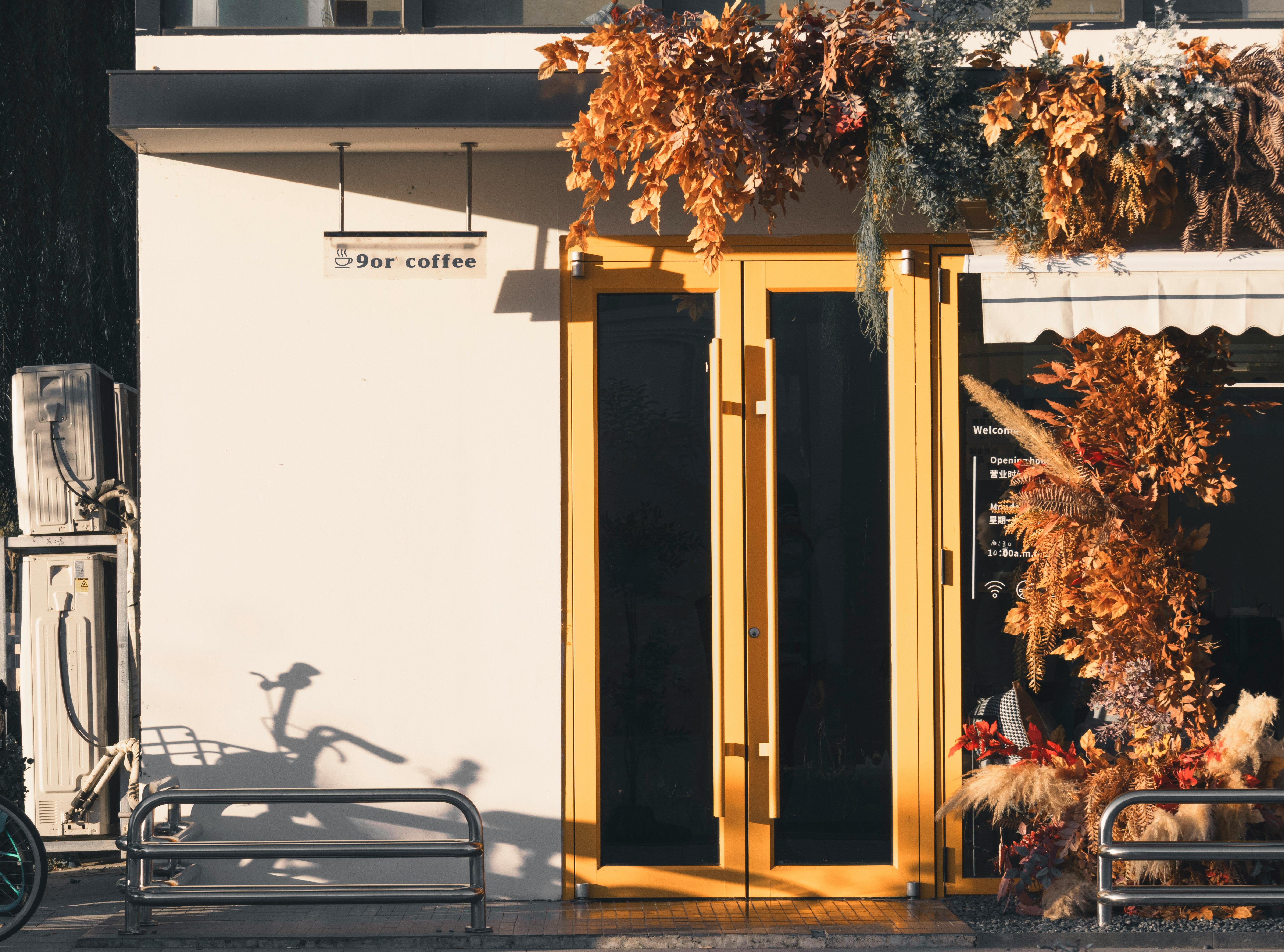 бесплатная Вход в кофейню, оформленный в теплых тонах, украшен осенними листьями и игрой теней. Стоковое фото