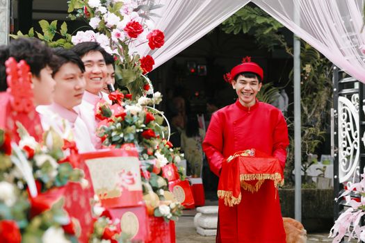 Joyful Asian groom in traditional attire at wedding ceremony adorned with vibrant floral decorations and happy guests.