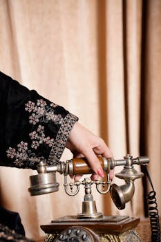 Close-up of an embroidered sleeve hand holding an antique vintage phone.