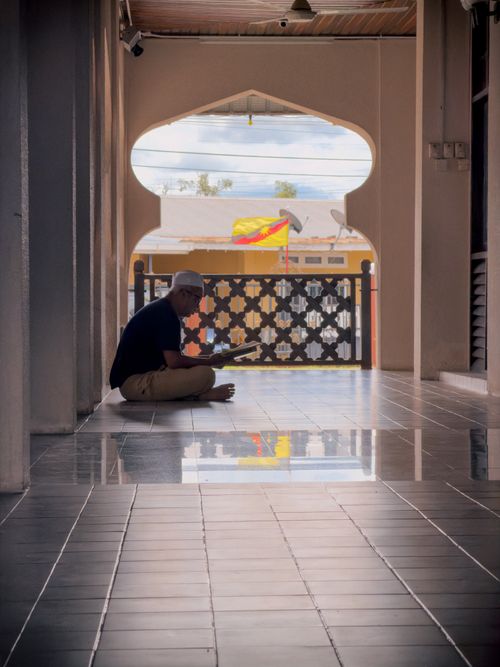 Free A serene moment of a man reading inside a mosque corridor in Sarawak, Malaysia. Stock Photo