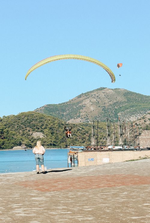 Free A paraglider soars over a picturesque lakeside with mountains in the background, capturing an adventurous moment. Stock Photo