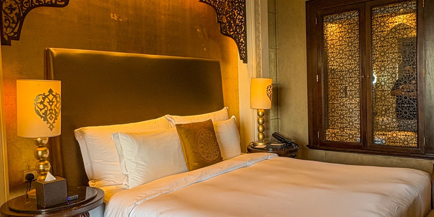 A neatly made bed in a bright hotel room in the late morning