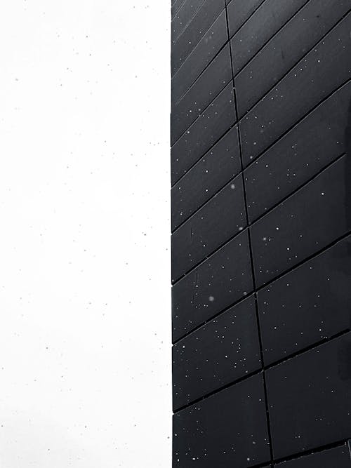 Low angle of wall of tall building with black modern cladding against white sky on snowy day