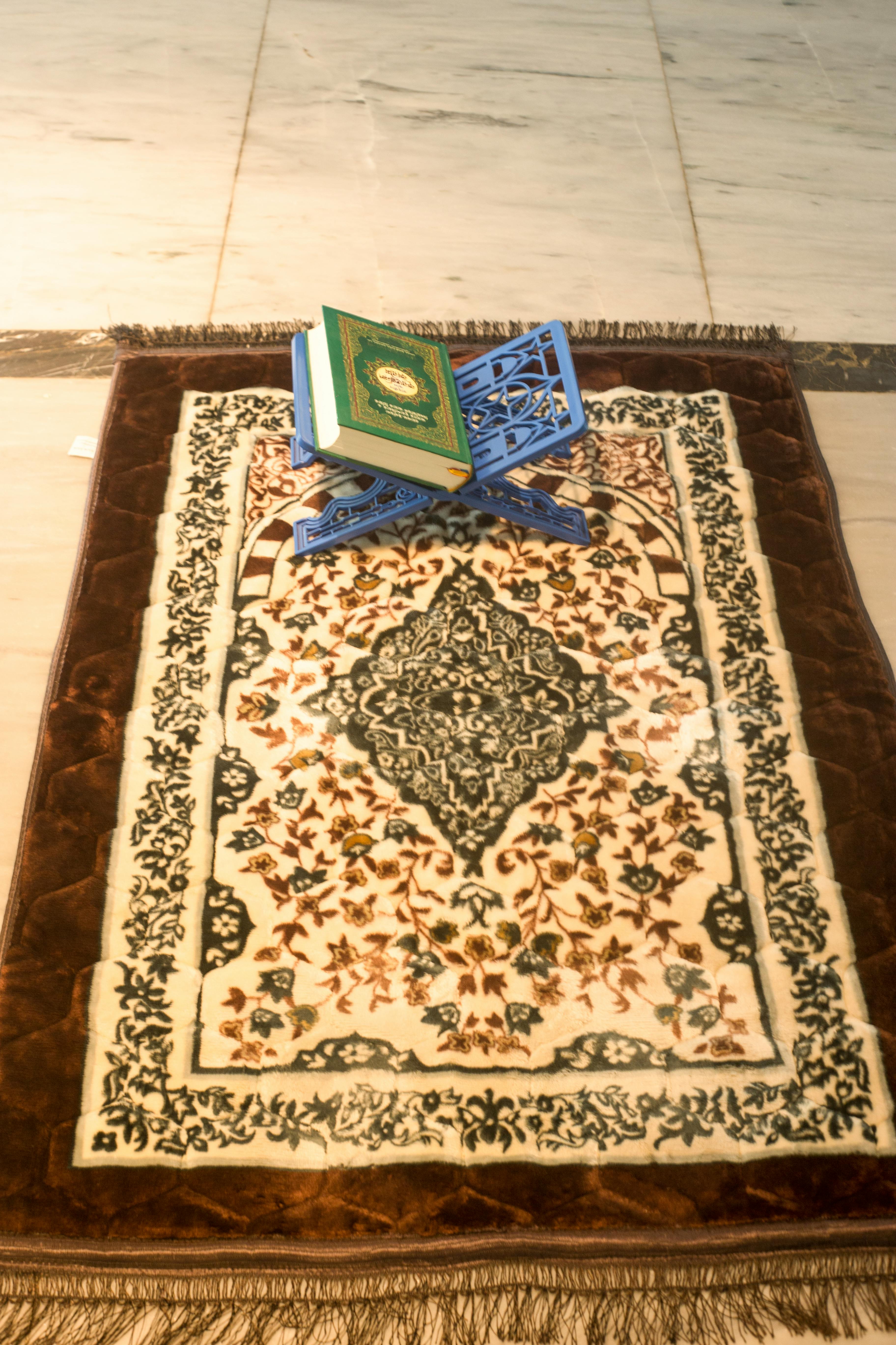 An open Quran resting on a wooden stand beside an Islamic prayer rug, a quiet space for reflection and salatul tawbah