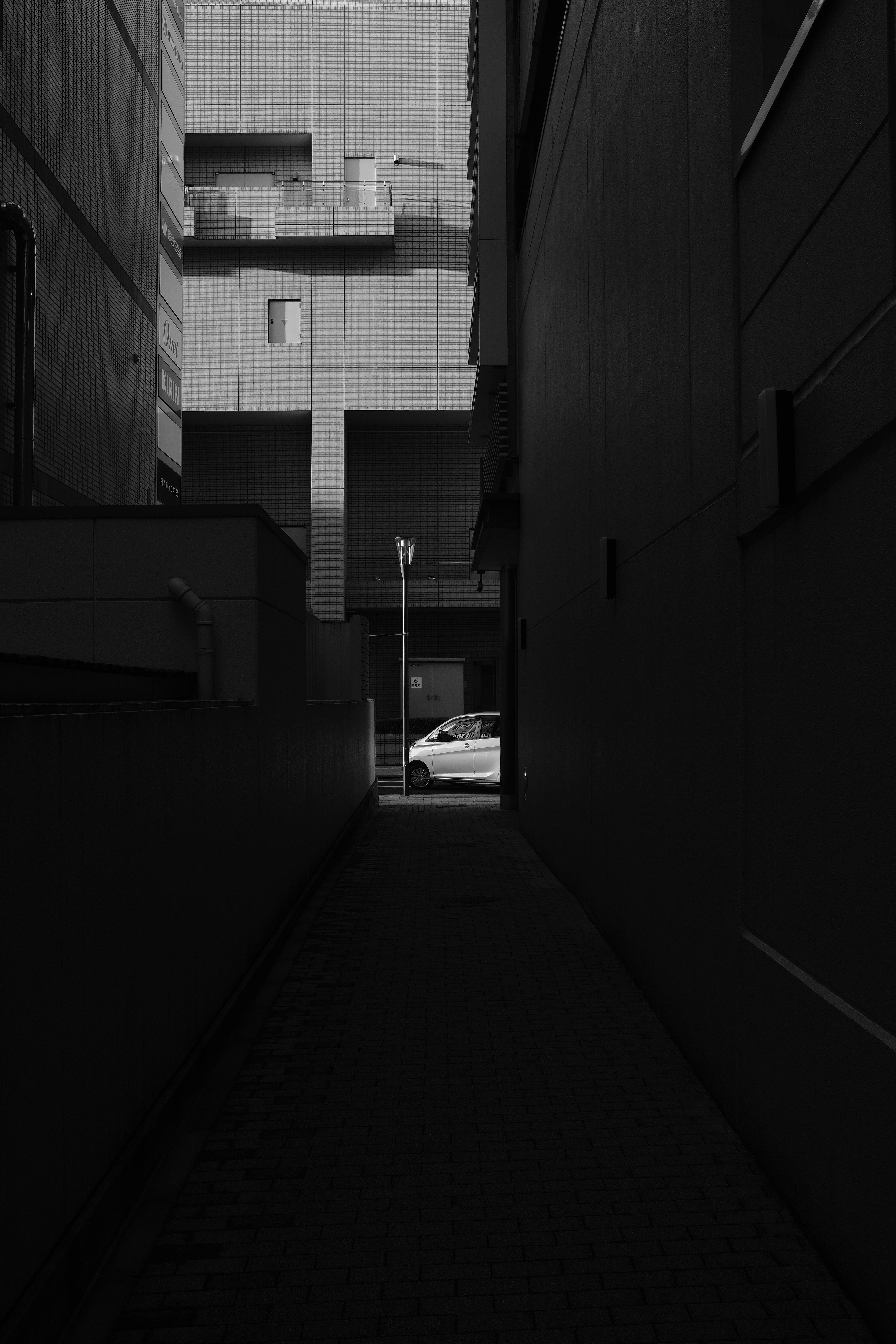 Gratuit Une photo en noir et blanc à l'atmosphère mélancolique, montrant une ruelle urbaine avec une voiture éclairée à la sortie. Photos