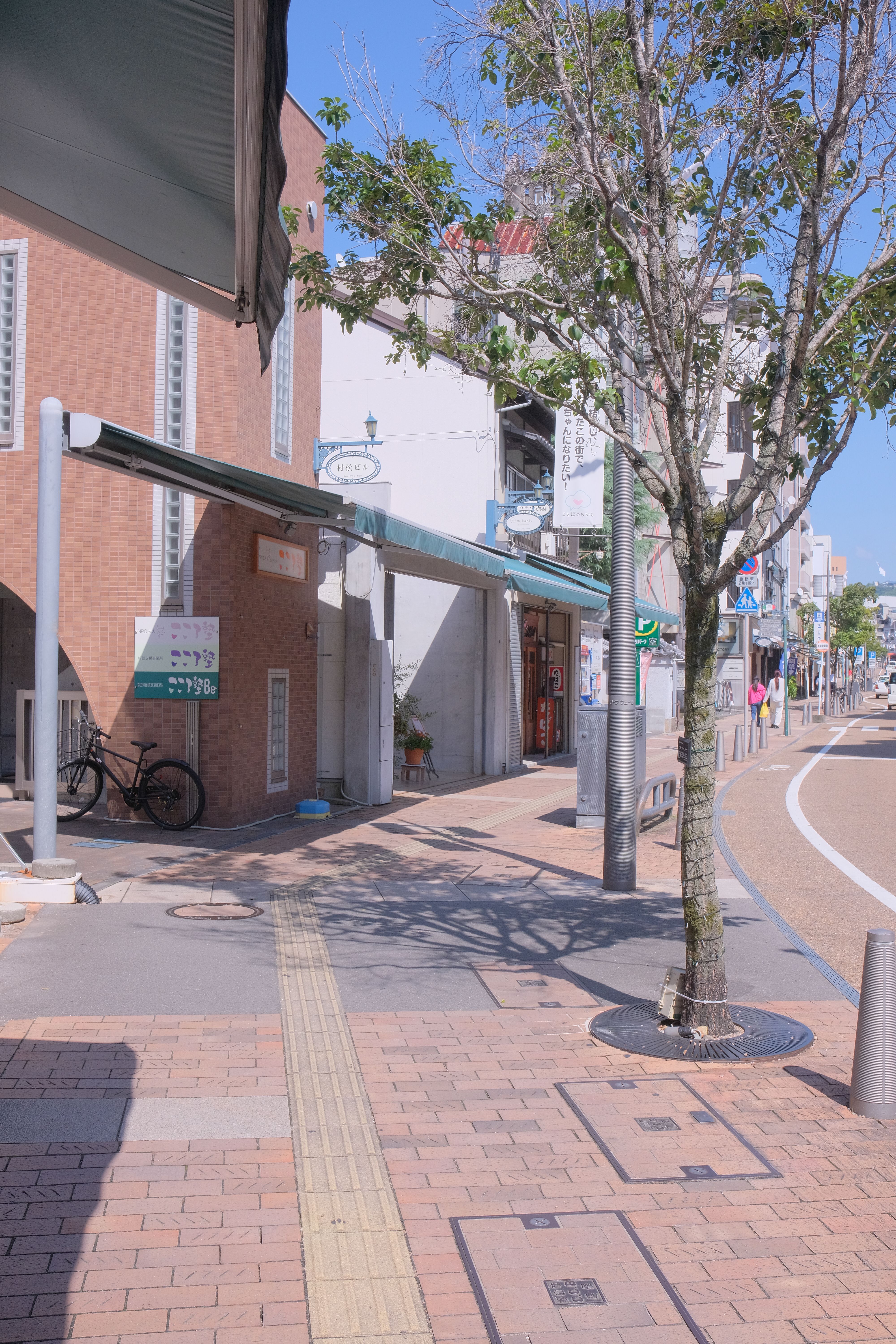A calm city street scene featuring a bicycle, trees, and modern architecture on a sunny day.