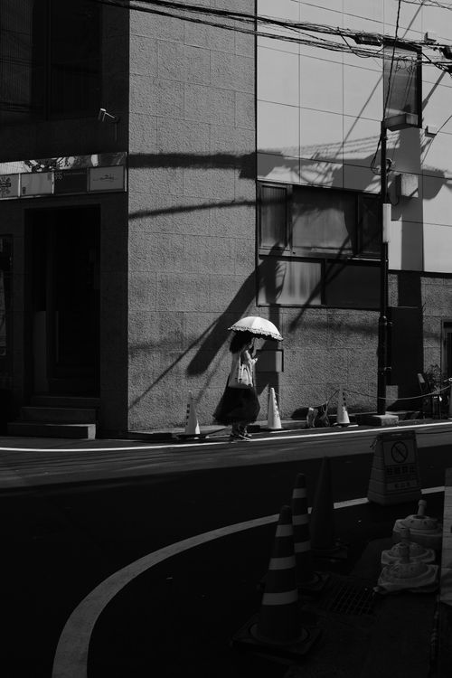 Free A person with an umbrella walks in shadows of urban architecture. Stock Photo